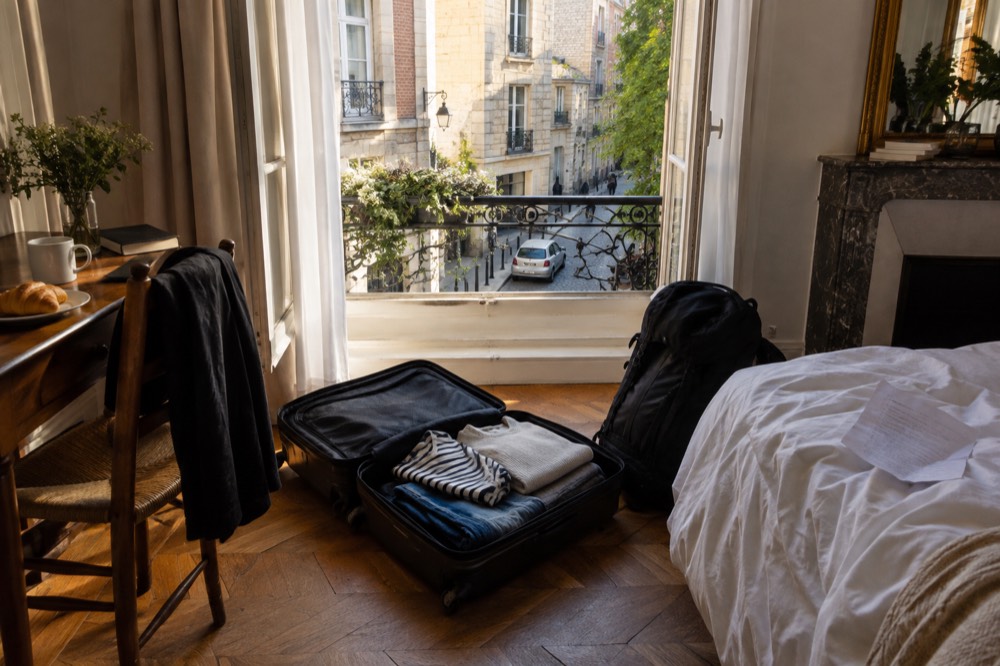 Une valise ouverte sur le sol d'une chambre d'hôtel avec un sac plein à côté, à l'heure du départ