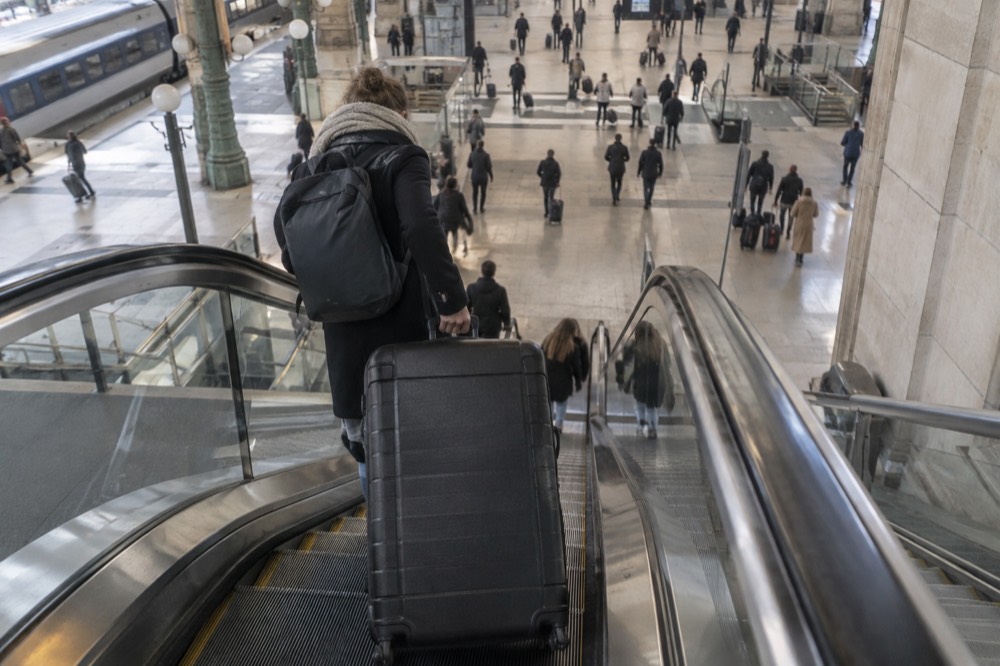 Un voyageur installant une valise sur un escalier mécanique descendant vers un niveau inférieur de la gare, à Paris