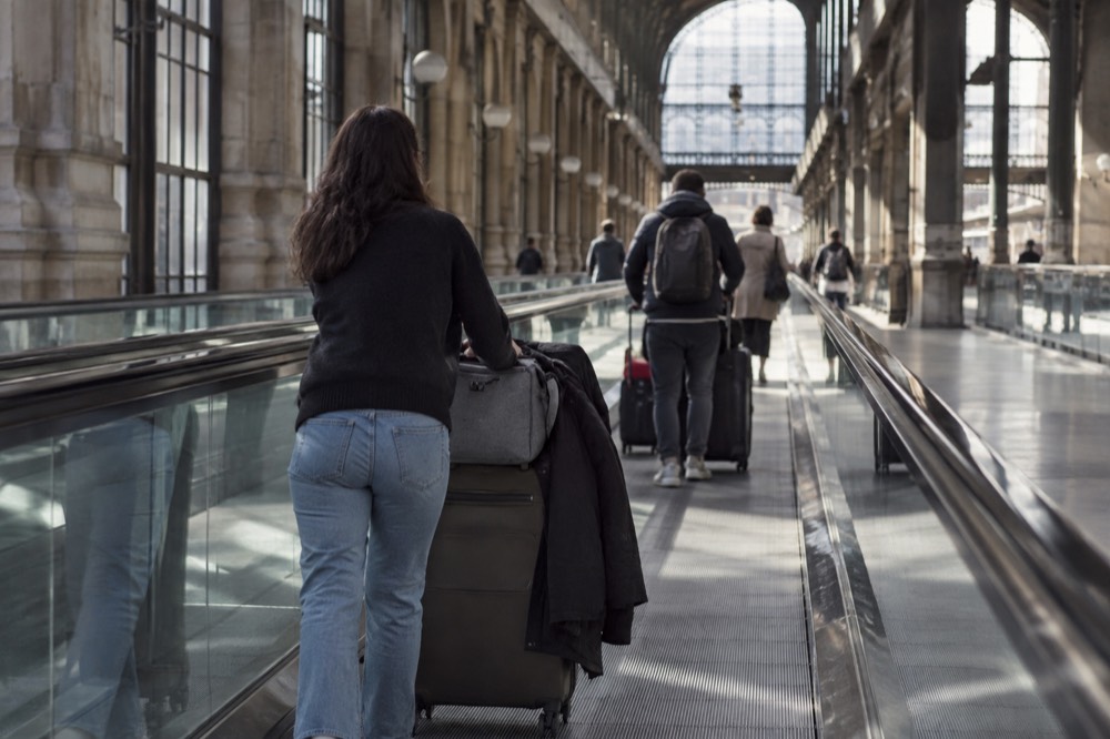 Voyageurs avec des chariots de bagages sur un trottoir roulant dans un couloir d'aéroport près de Paris