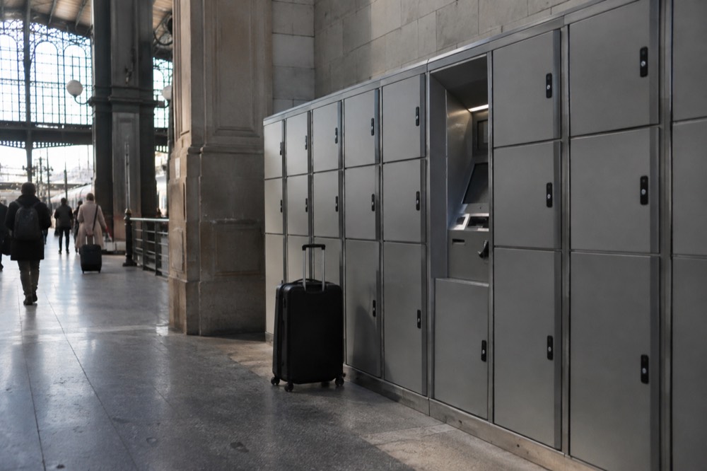 Des casiers à bagages automatisés alignés le long d'un mur de gare, avec une valise à roulettes posée à côté