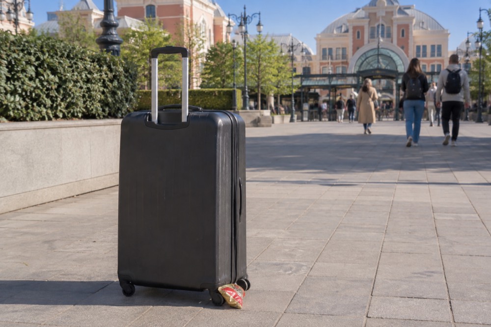 Une grande valise posée à côté d'une arche d'entrée de parc à thème sous un ciel dégagé