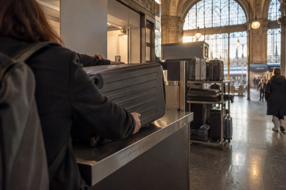 Un voyageur remettant une valise à un membre du personnel à un comptoir de consigne à bagages dans une gare