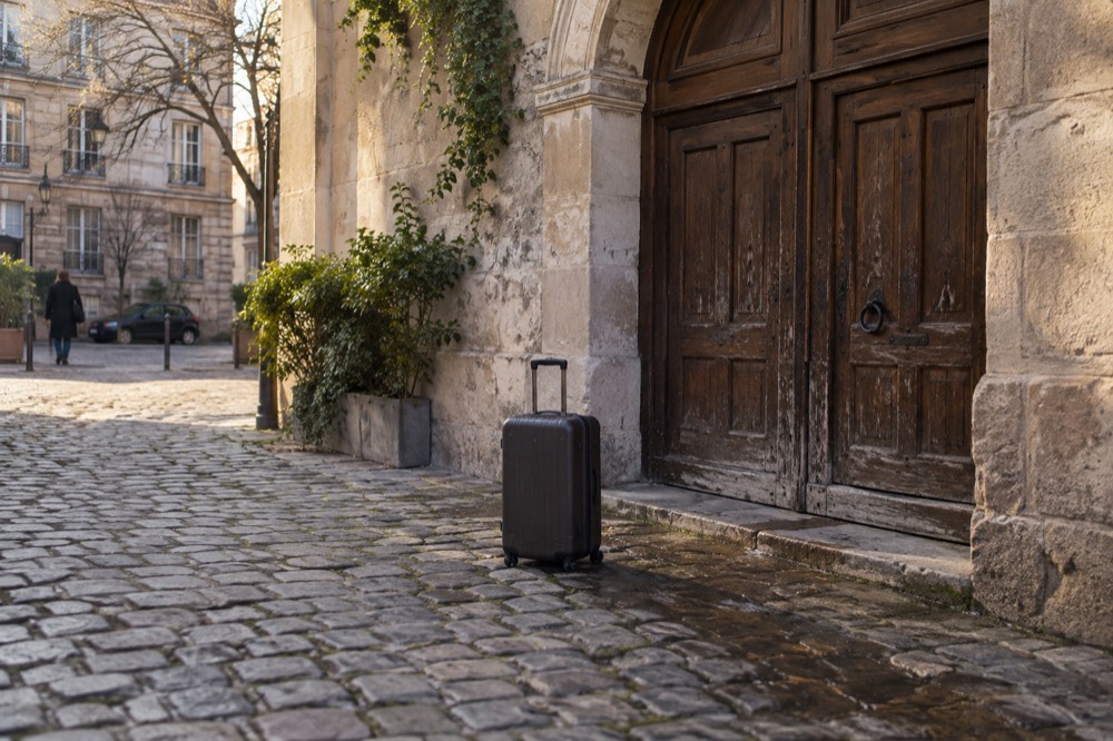 Une valise devant la porte en bois fermée d'un petit hôtel parisien à la façade en pierre