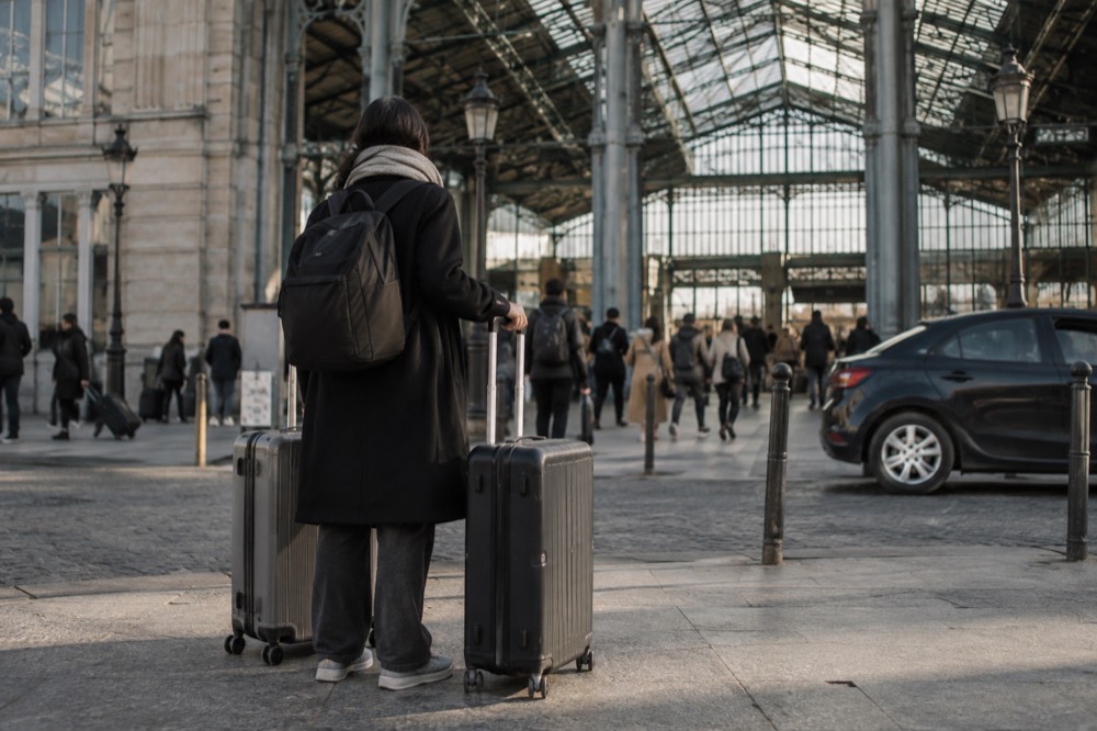 A traveller with two cases waiting under the high roof above the departures entrance at Gare du Nord