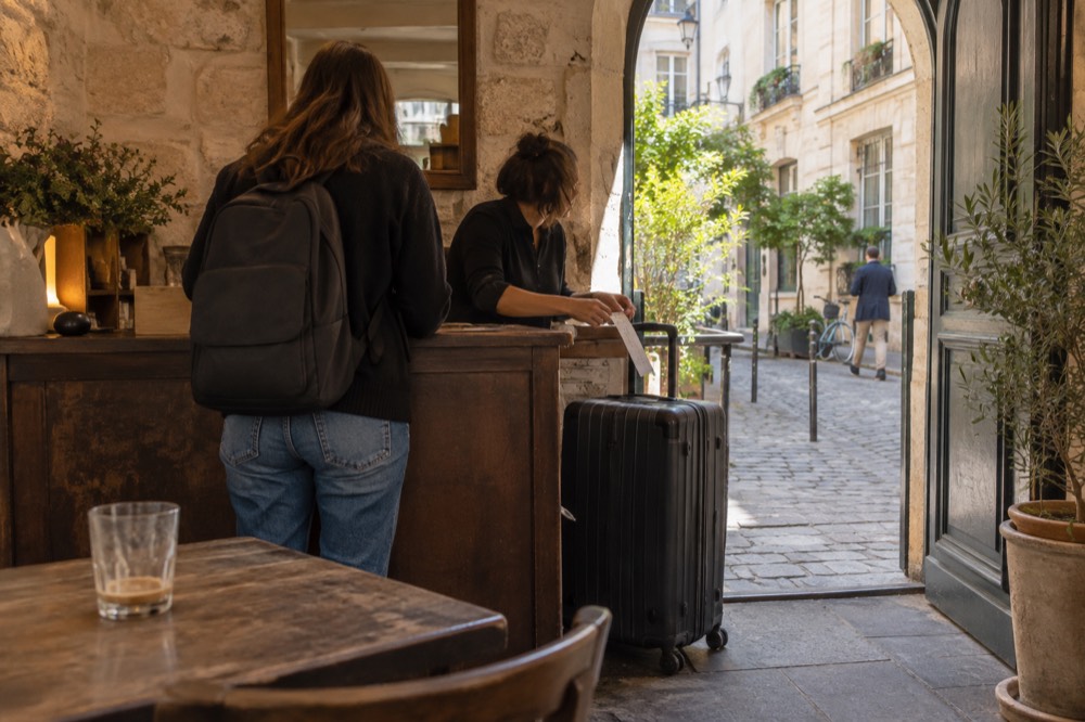 Intérieur lumineux d'un café avec un comptoir tenu par du personnel, où une valise est remise et étiquetée derrière le bar