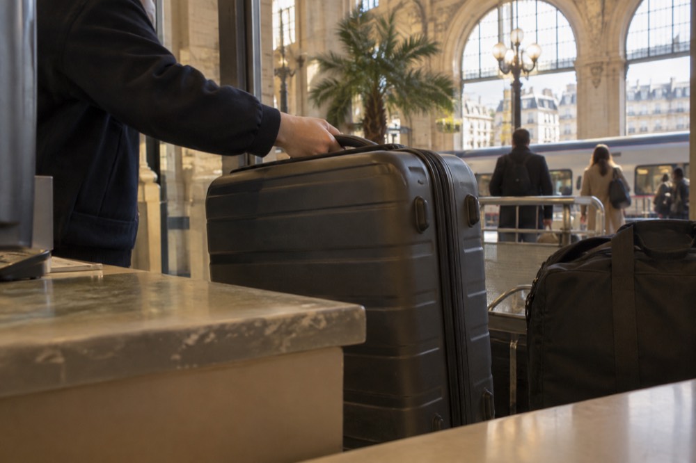 A storage point worker placing a labelled suitcase behind a reception desk
