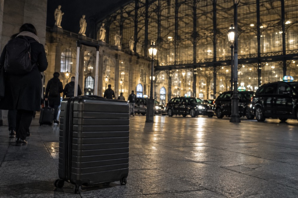 Valises sur le trottoir devant la Gare du Nord la nuit, avec des lumières de taxi en arrière-plan