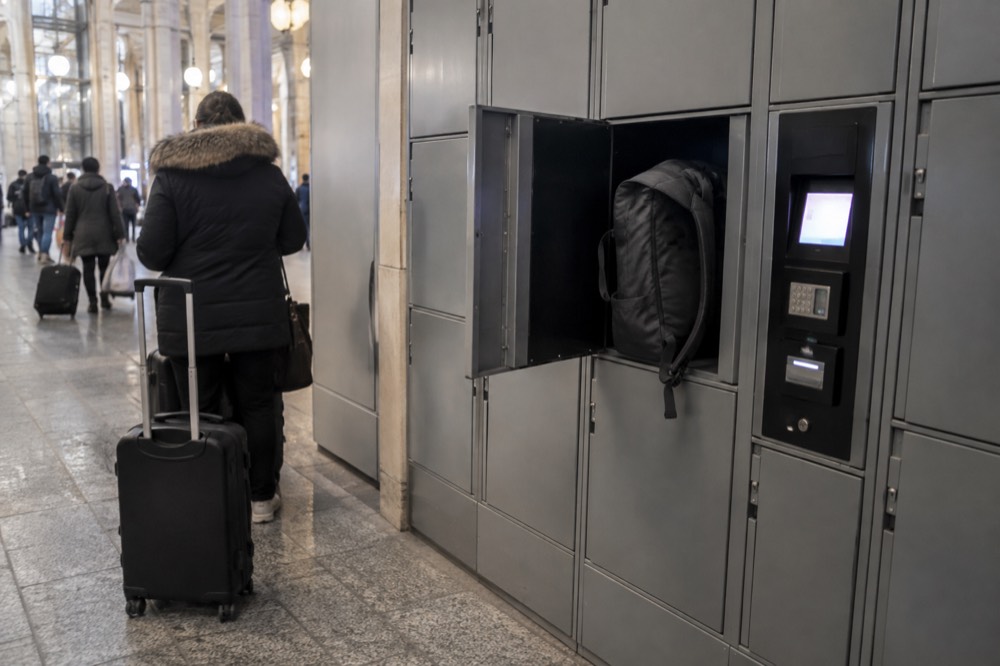 Une rangée de casiers à bagages en libre-service dans un couloir de gare, avec un terminal de paiement à côté