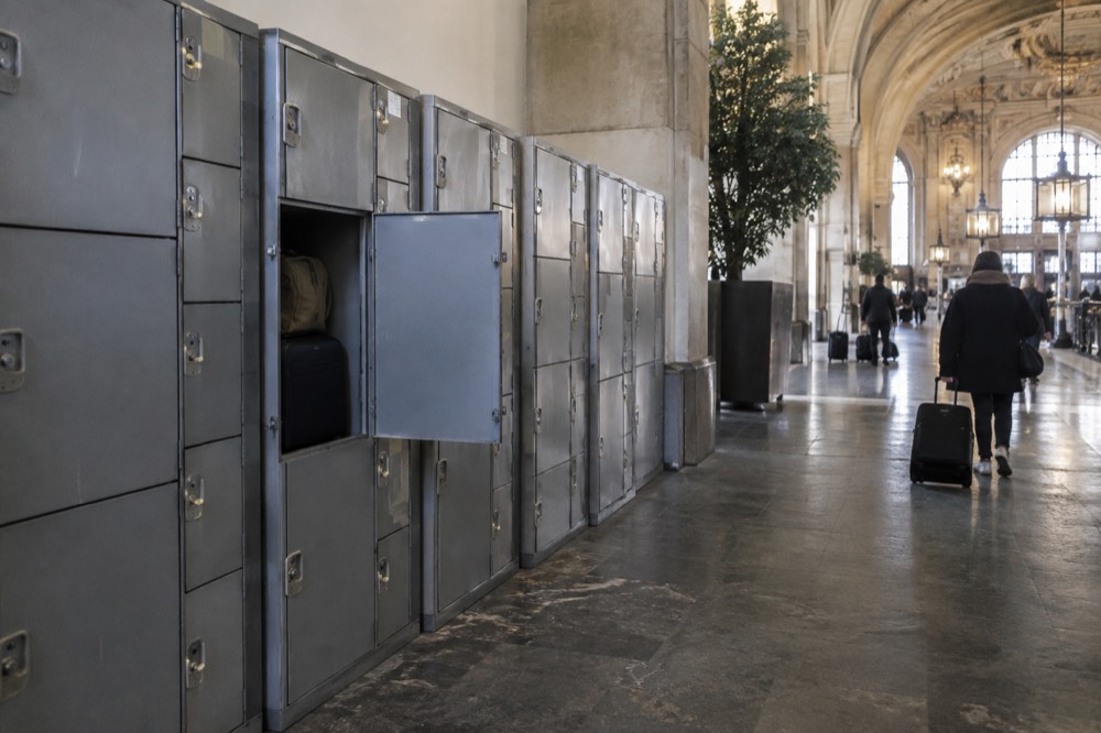 A row of grey station luggage lockers of three different sizes along a corridor wall