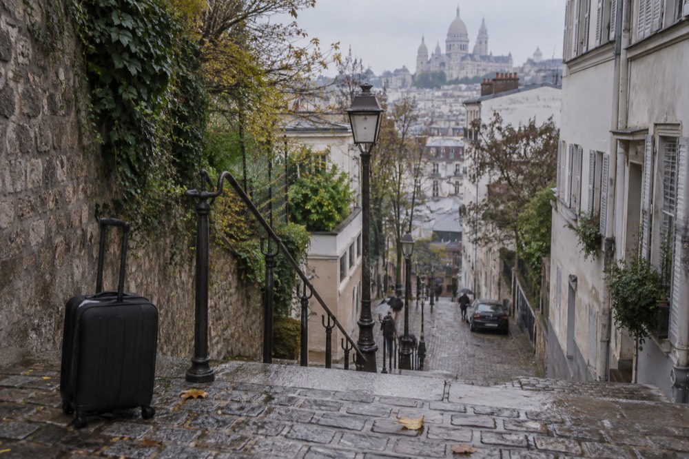 Steps rising towards a white domed basilica on a Paris hill, with a suitcase resting at the bottom of the staircase