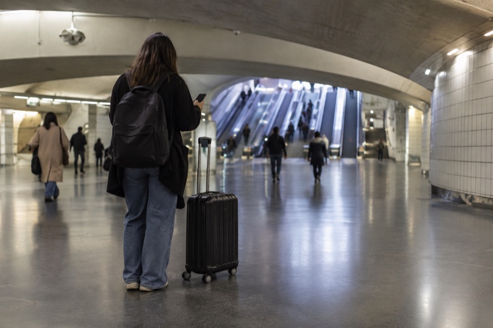 Un voyageur tenant un téléphone à côté d'une valise dans le hall d'une gare parisienne