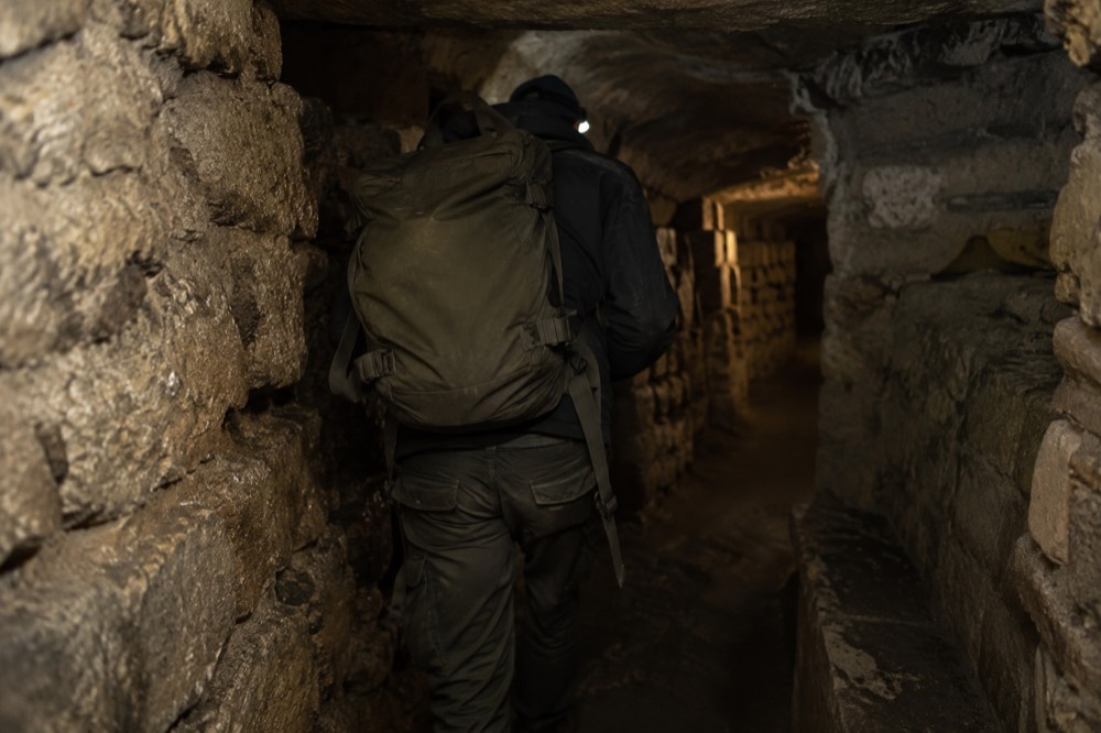 Un sac à dos porté dans un étroit tunnel de pierre des Catacombes de Paris