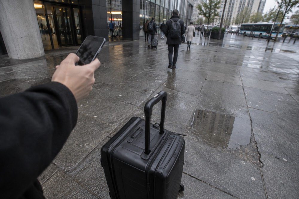 A phone held in one hand above a suitcase on a Paris street corner